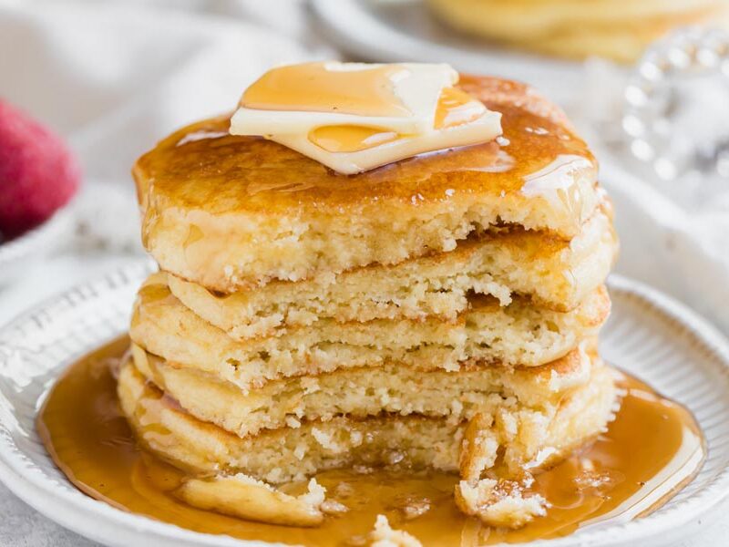 A bite missing from a stack of pancakes covered with syrup.
