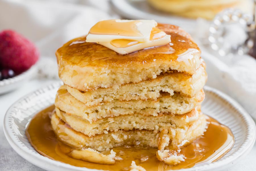 A bite missing from a stack of pancakes covered with syrup.