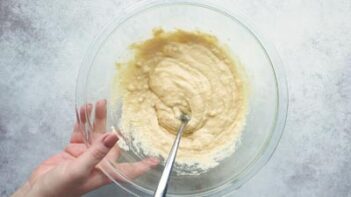 Thick pancake batter in a bowl with a hand grabbing the bowl.