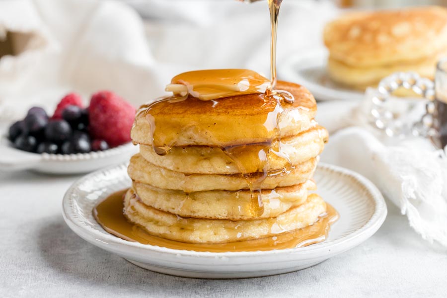 Syrup drizzling down a stack of pancakes on a plate.