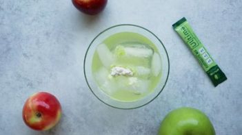 ingredients for a green drink in a glass with two apples next to the glass