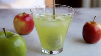 stirring a bright green cocktail with apples surrounding