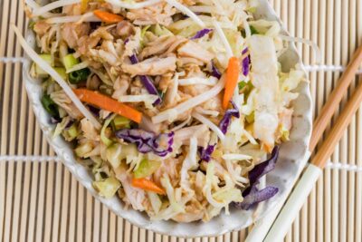 A bowl of Chinese chicken salad with canned chicken, cabbage, bean sprouts, carrots, green onions, and sesame dressing.