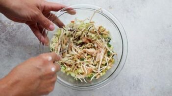 Tossing Chinese chicken salad ingredients together until evenly coated with the sesame dressing.