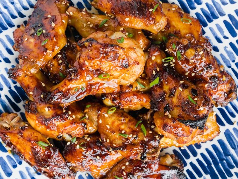 Looking down onto a plate of Asian chicken wings in a soy based sauce with green onions on top.