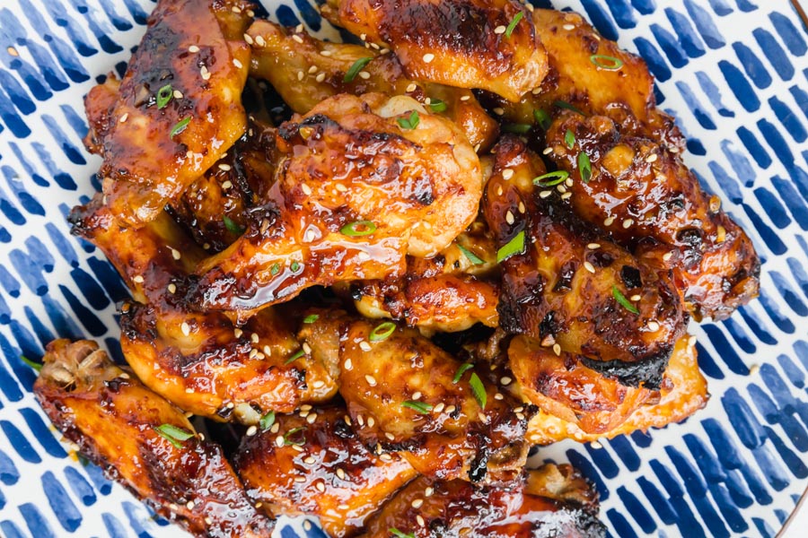 Looking down onto a plate of Asian chicken wings in a soy based sauce with green onions on top.