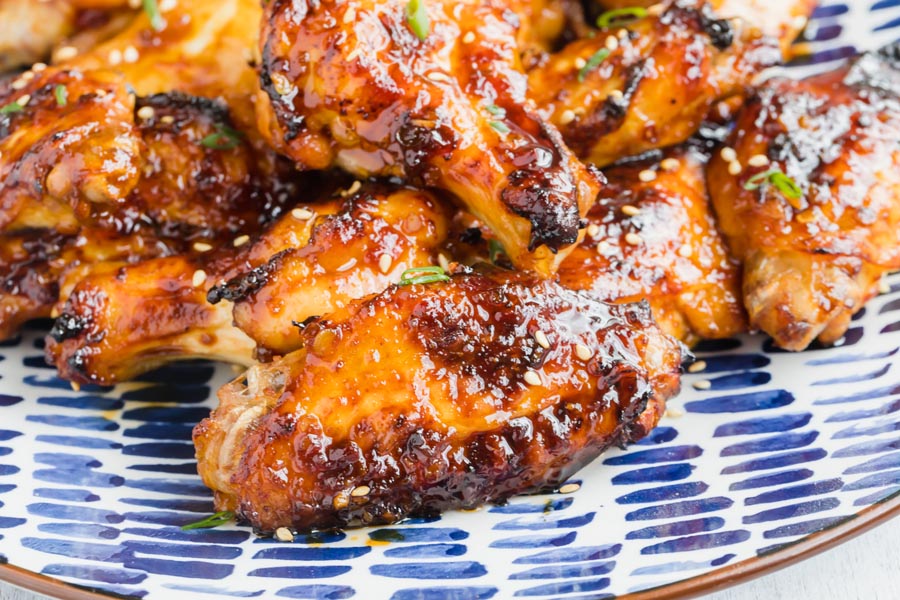A pile of Asian chicken wings on a blue and white plate. The shot is focused on a flat or wingette with a caramelized sauce coated on the outside.
