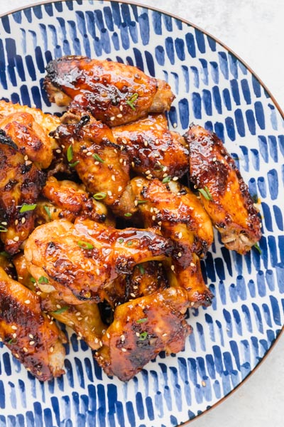 A plate of chili garlic wings piled on each other and topped with sesame seeds and sliced green onions.