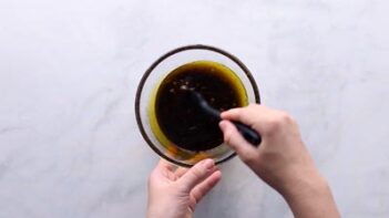 A hand stirring a soy based marinade with a spoon.