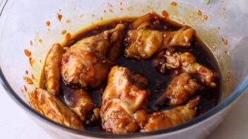 Raw party wings marinating in a bowl with a soy and chili based sauce.