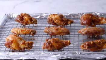 Raw marinated chicken wings on top of a wire rack over a foil lined tray.