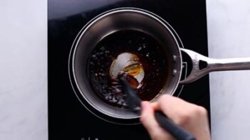 A hand stirring a soy based glaze over a burner,