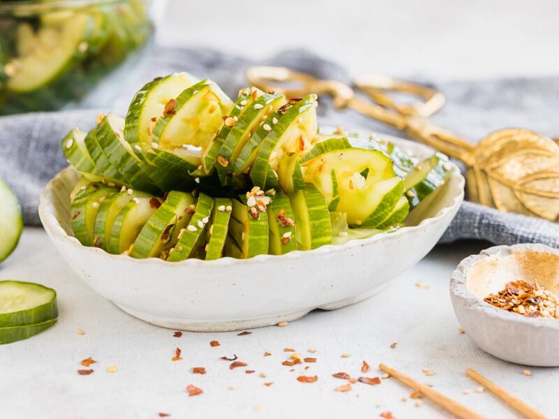 a bowl of cucumbers cut up in a bowl with a slices cucumber and spices next to it