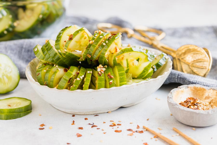 a bowl of cucumbers cut up in a bowl with a slices cucumber and spices next to it