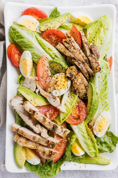 a salad on a rectangular plate with a light vinaigrette on top and pepper