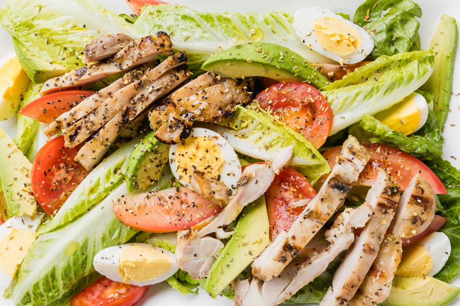 sliced chicken, egg, avocado and tomatoes mixed with hearts of romaine on a plate