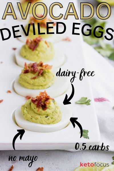 A row of avocado deviled eggs topped with bacon on a serving dish.