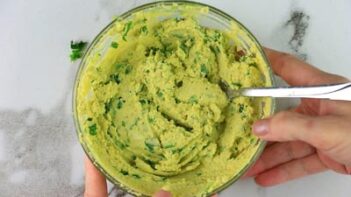 Hands holding a mixing bowl filled with an avocado yolk mixture for deviled eggs.