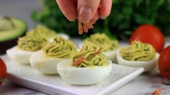 Sprinkling crumbled bacon on top of avocado deviled eggs.