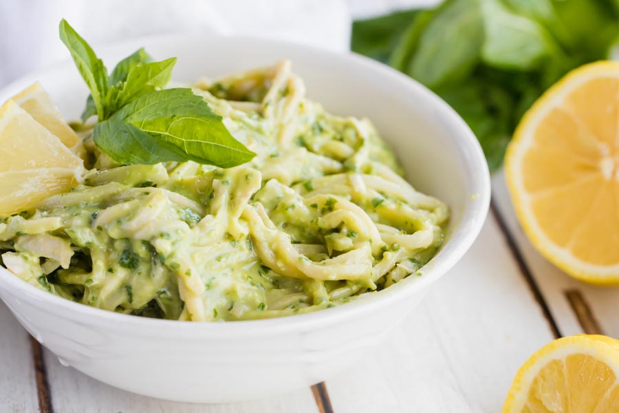 a white bowl of spaghetti noodles mixed a chicken and creamy pesto sauce