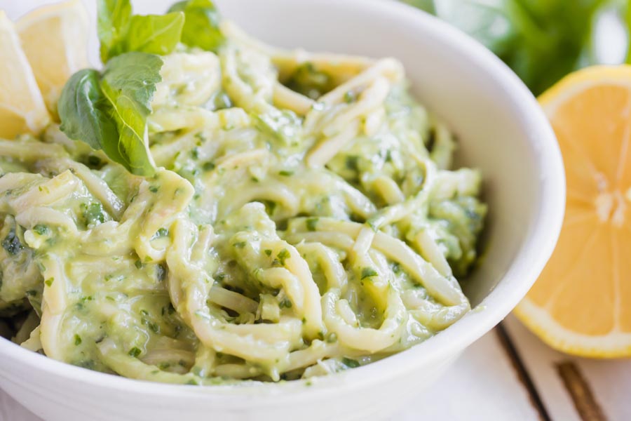avocado pesto sauce mixed into noodles and topped with more basil leaves