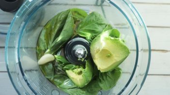 chunks of avocado on a bed of basil leaves in a food processor