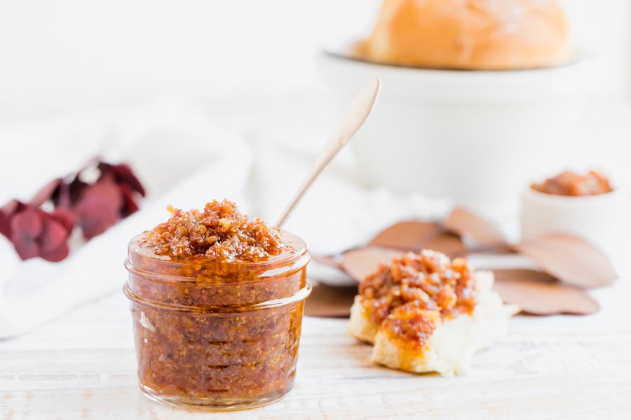 bacon jam in a small jar next to a roll with bacon jam on it