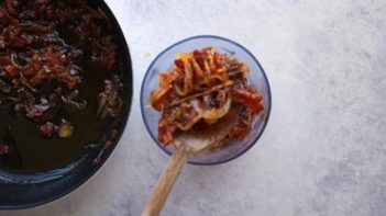 a wooden spoon holding bacon and onion mixture