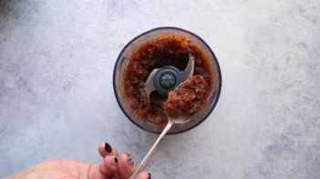 holding a spoon of bacon jam over a food processor