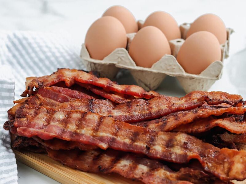 cooked bacon with grill marks in front of whole eggs