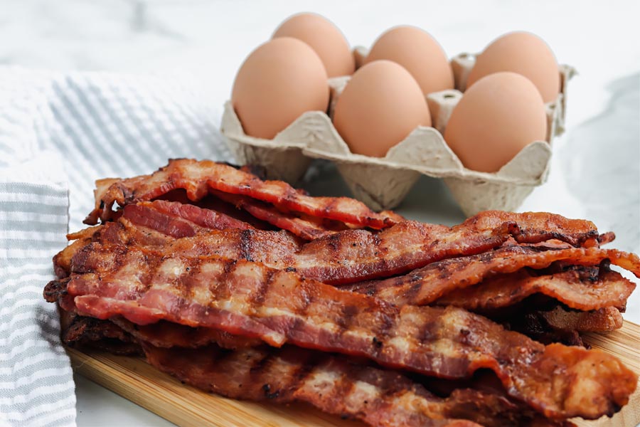 cooked bacon with grill marks in front of whole eggs