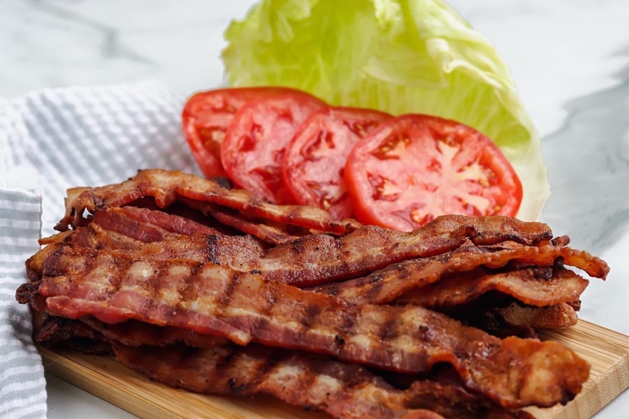 crispy grilled bacon on a butcher block with sliced tomatoes and lettuce