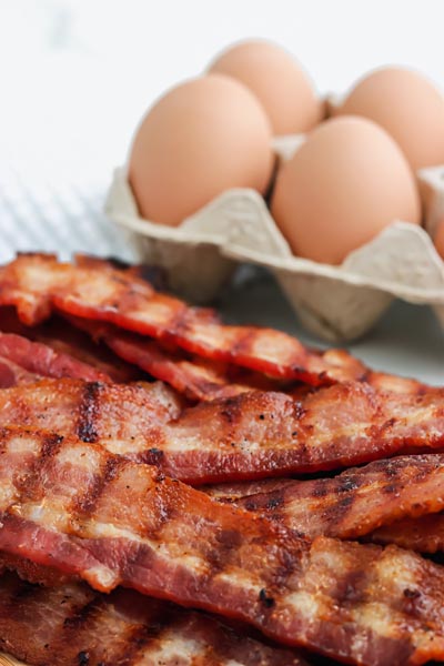 cooked bacon in front of a carton of eggs