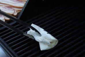 cleaning with grill with tongs holding a oil soaked paper towel
