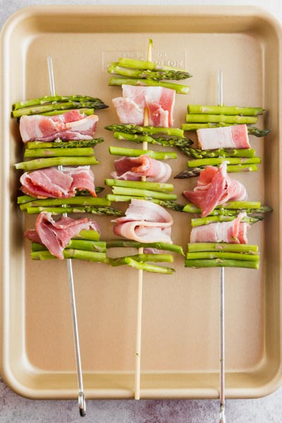 three uncooked bacon asparagus kebabs on a pan