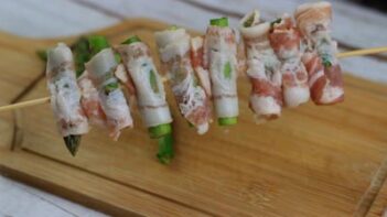 raw strips of bacon wrapped individually wrapped around a small cut of asparagus on a skewer