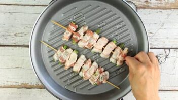 placing bacon wrapped asparagus skewers on a baking disb