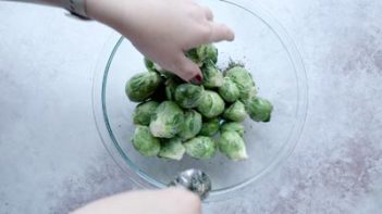 tossing whole fresh brussels sprouts with salt and pepper in a bowl with a spoon