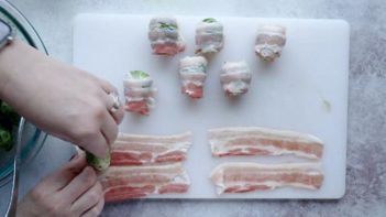 rolling a brussels sprout with a strip of bacon on a cutting board