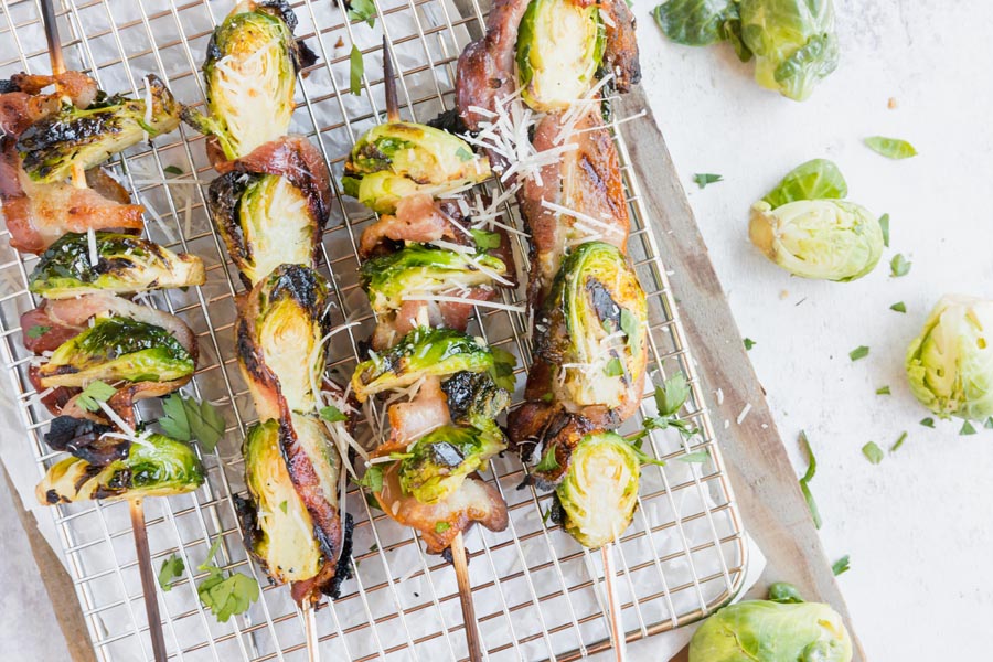 crispy grilled brussels sprouts on a skewer wrapped in bacon with whole sprouts nearby