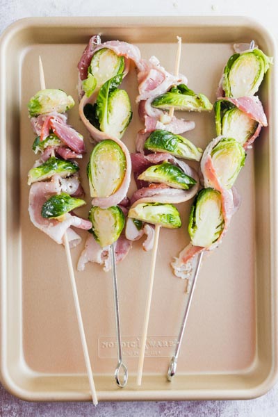 uncooked bacon and brussels sprouts kebabs on a baking tray