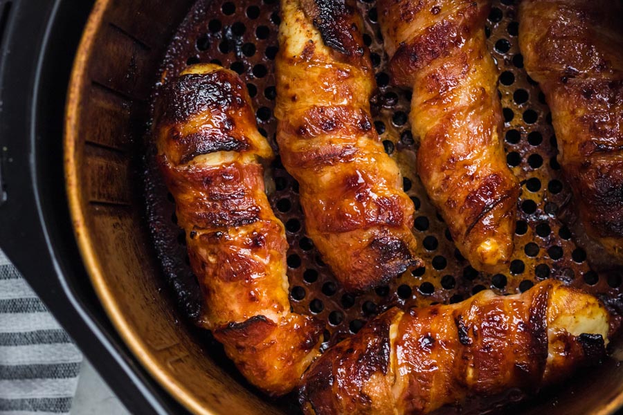 Five bacon wrapped chicken tenders in an air fryer basket. Bacon is crispy and chicken is juicy.