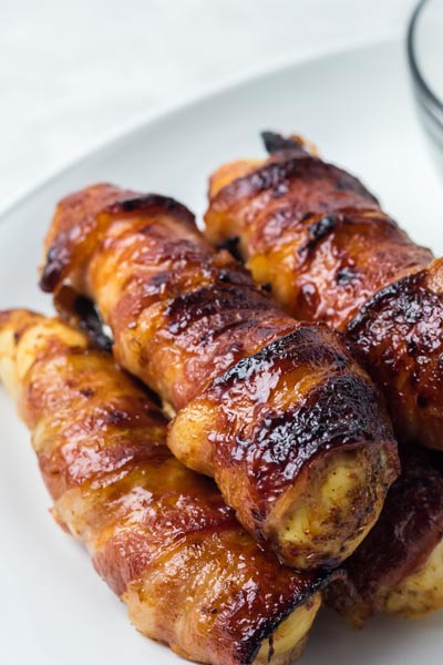 Crispy bacon is wrapped around baked chicken strips on a plate.