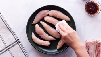 Patting chicken tenders dry sitting on a black plate with a paper towel.