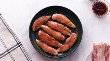 A black plate with raw chicken tenderloins coated with seasoning.