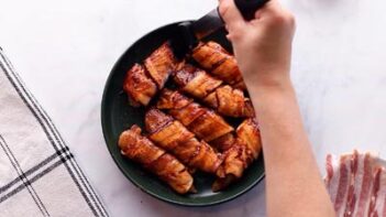 Brushing bbq sauce onto bacon wrapped chicken with a black silicone brush.