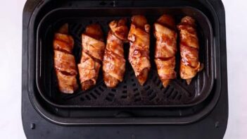 Raw bacon wrapped tenders coated with bbq sauce sitting in an air fryer basket.