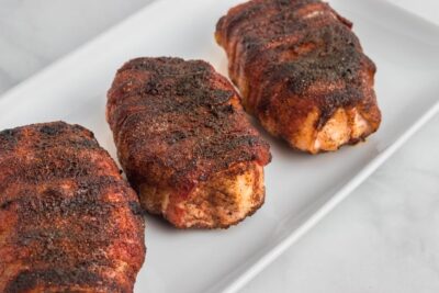 Pork chops wrapped in crispy bacon on a white platter.