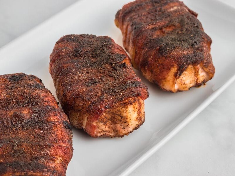 Pork chops wrapped in crispy bacon on a white platter.