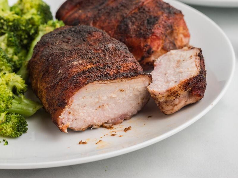A slice of bacon wrapped pork chop off to the side of a plate to show how juicy it is inside.